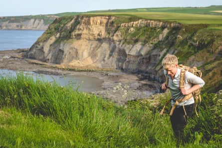 A young man with a rucksack walking on a cliff by the sea
