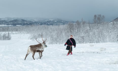 A Sami man leading a reindeer across a snowy landscape