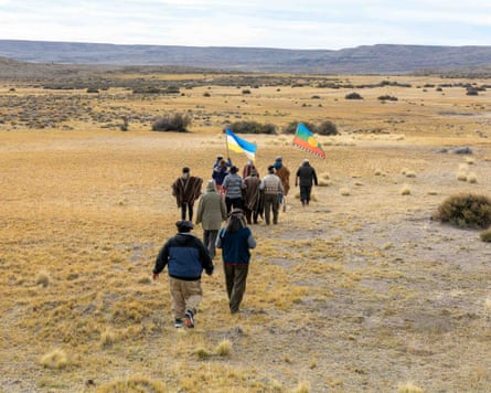 A group of people carrying two flags walk away from the camera across grasslands.