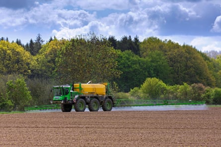 A truck with a tank moves across a field with arms spraying the earth behind it.