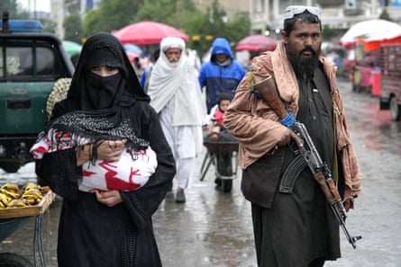 An Afghan woman walks through the old market as a Taliban fighter stands guard, in downtown Kabul 3 May 2022.