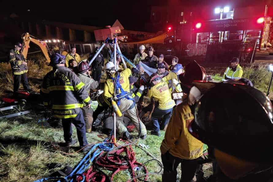 Emergency crew work in a field at night to free a man in a pipe.