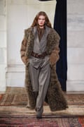 Model walks on catwalk in baggy suit and fur coat.