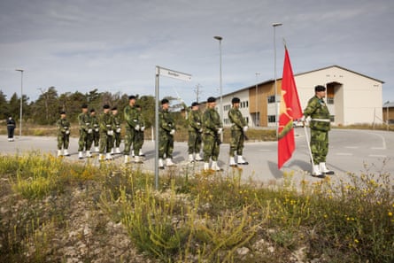 Small parade of soldiers marching along a street before an officer holding a large ceremonial flag