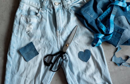 A pair of jeans being repaired with patches, with a pair of scissors and a measuring tape lying on top