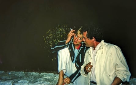 A woman and a man at night sitting on a wall smoking