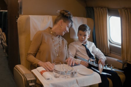 A woman and a boy sitting on a plane with a table set for a meal