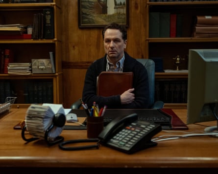 Matthew Rhys sitting a desk holding a folder