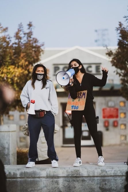 Two women stand on a concrete berm, holding megaphones and a sign.