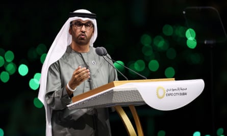 Sultan Al Jaber at a podium in front of a dark backdrop lit by green 