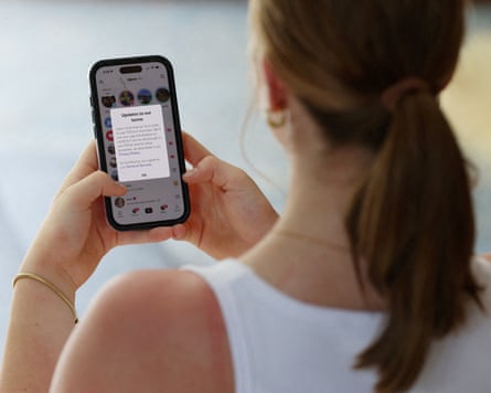 A teenager poses holding a mobile phone displaying a message from TikTok