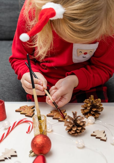A child paints pine cones and wooden Christmas tree decorations at home.