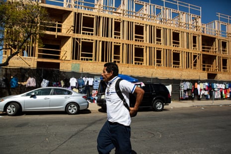 A man in a white shirt wearing a backpack walks in front of a large wooden construction site