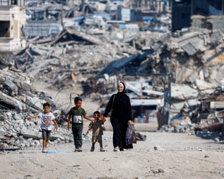 A woman and three children walking past destroyed buildings and piles of rubble