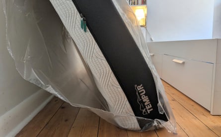 A Tempur Pro Plus SmartCool mattress on its side against a wall. It is still in its plastic wrapping