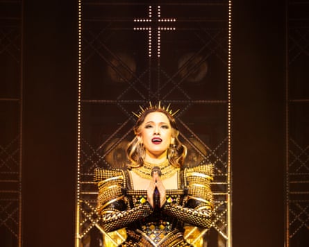 Sonim in a gold costume, singing while she kneels with her hands in a prayer position.