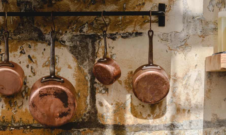 Copper pots and pans hanging against a weathered stone wall