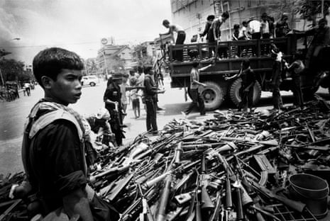 black and white picture from 1975 of a child standing in front of a pile of guns in Phnom Penh.