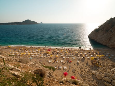 A sandy beach with rows of sunloungers and an island in the distance