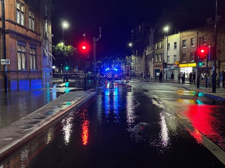 A London street at night with water flooding the road and spilling onto the pavement
