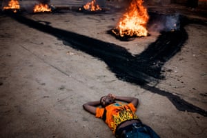 An opposition supporter lays on the street, unharmed, as he protests near a burning barricade in the Kibera shanty town of Nairobi, Kenya