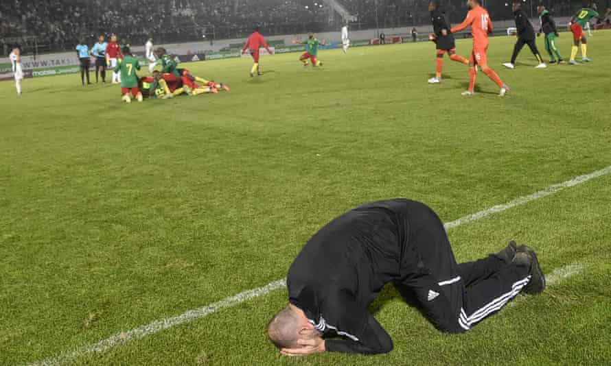 Algeria’s coach Djamel Belmadi reacts to their defeat while Cameroon players celebrate in the background.
