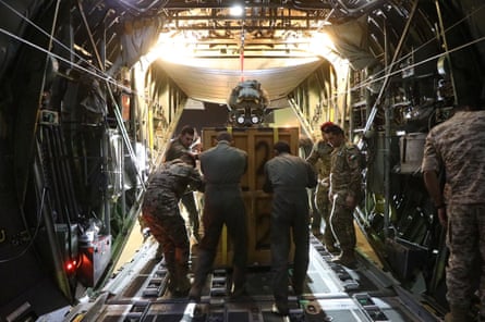رجال يرتدون الزي العسكري يدفعون حاوية إلى خارج الجزء الخلفي من الطائرة.
