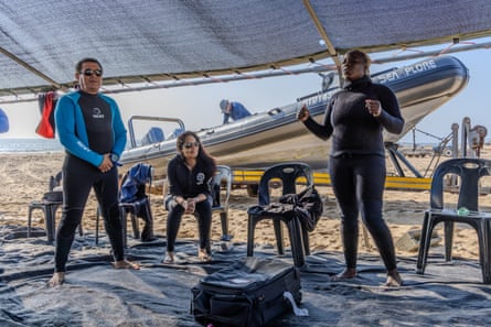 Silindile Mbuyazi stands under a tarpaulin on the beach with Noel Kok and Pragna Parsotam-Kok, with a speedboat in the background