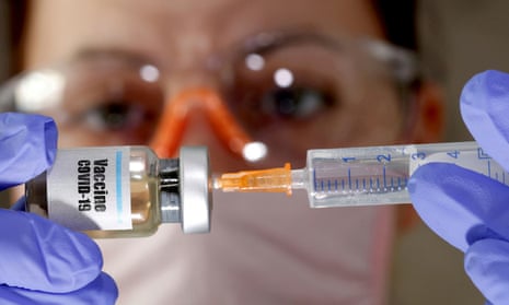 woman holds a small bottle labeled with a “Vaccine COVID-19” sticker and a medical syringe