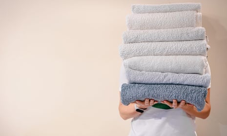 Woman holding a stack of clean white bath towels on light background