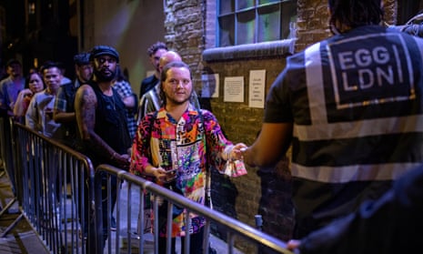 A man in a colourful shirt showing tickets to a bouncer at the head of a queue outside