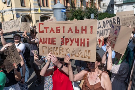 Protesters hold up handwritten cardboard signs in a large crowd in front of public buildings.