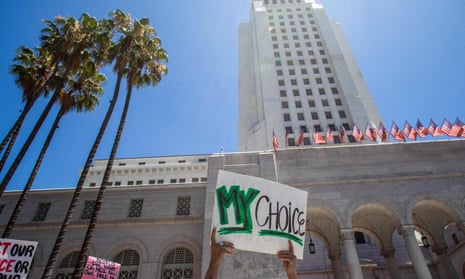 Hands hold up a sign saying 'My choice' in front of a tall white stone building with palm trees in front.