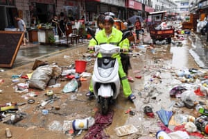 Huangshan, China: a man rides a scooter down a street strewn with rubbish after heavy rains caused flooding