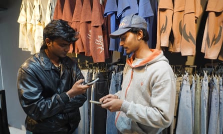 Two men holding mobile phones stand next to racks of clothes.