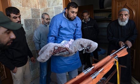 A man carries a child’s body wrapped in a blanket to be placed on a stretcher