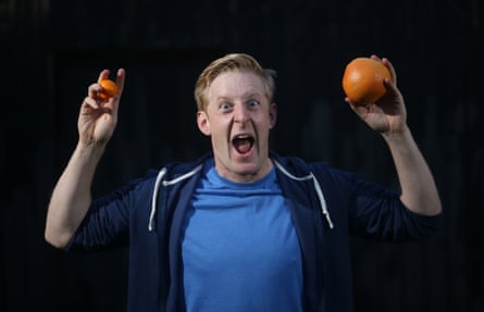 Michael Patrick shouting at the camera while holding a small satsuma and a large orange