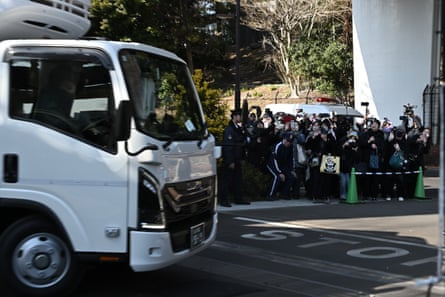 A crowd of people watch and photograph a truck