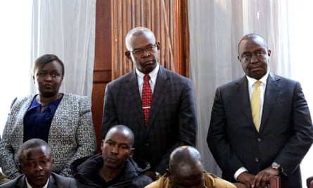 A formal group photo of one woman and two men standing behind some other people