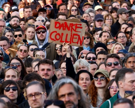 A person in the middle of a crowd holds up a homemade placard with the words 'Danke Collien'
