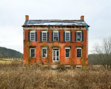 a dilapidated but grand-looking red-brick house, with a row of five windows on its upper storey, in a field