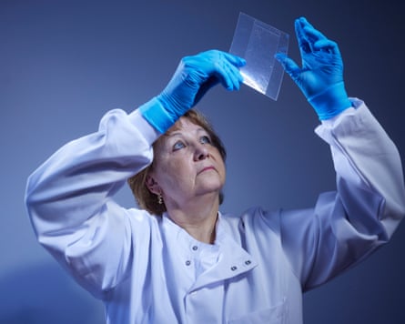 Angela Gallop in lab coat and gloves holding a sample to a light source