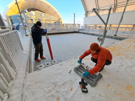 A large square pool covered in ice, with two people working on and next to it.