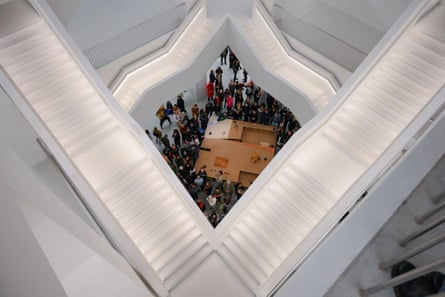 White staircases in geometric shapes like an Escher painting seen from above, with people in an atrium below.