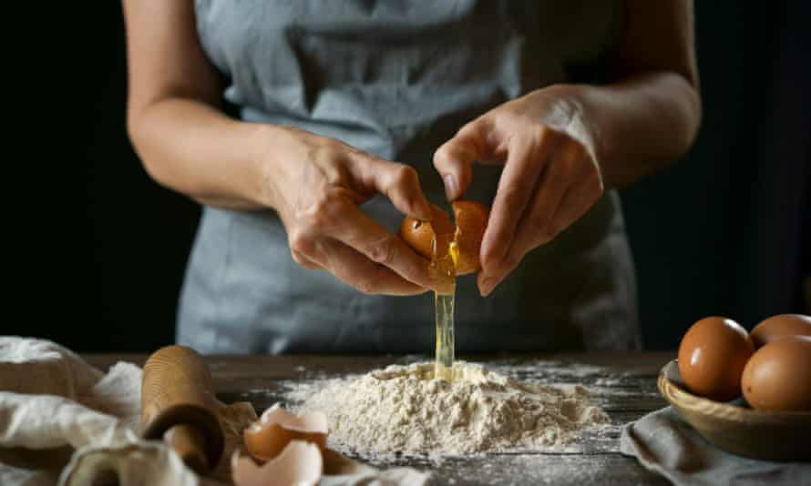 woman cracking egg over flour