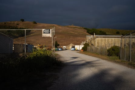 Long shadows over road leading past chain-link fence to golden hill.