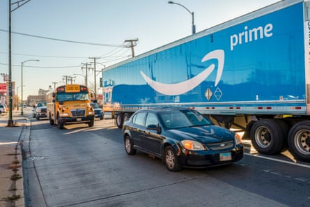 A large blue truck with the Amazon prime symbol drives on the road with other cars and school pus