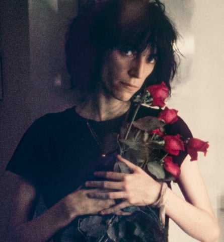 She holds a bunch of wilting red roses and looks impassively at the camera