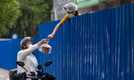 A delivery person receives a bag of take-away food over a constructed barrier during a lockdown in China in June 2022.