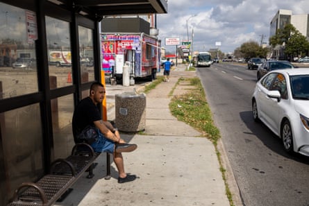 A man waits for a bus as cars are seen close by